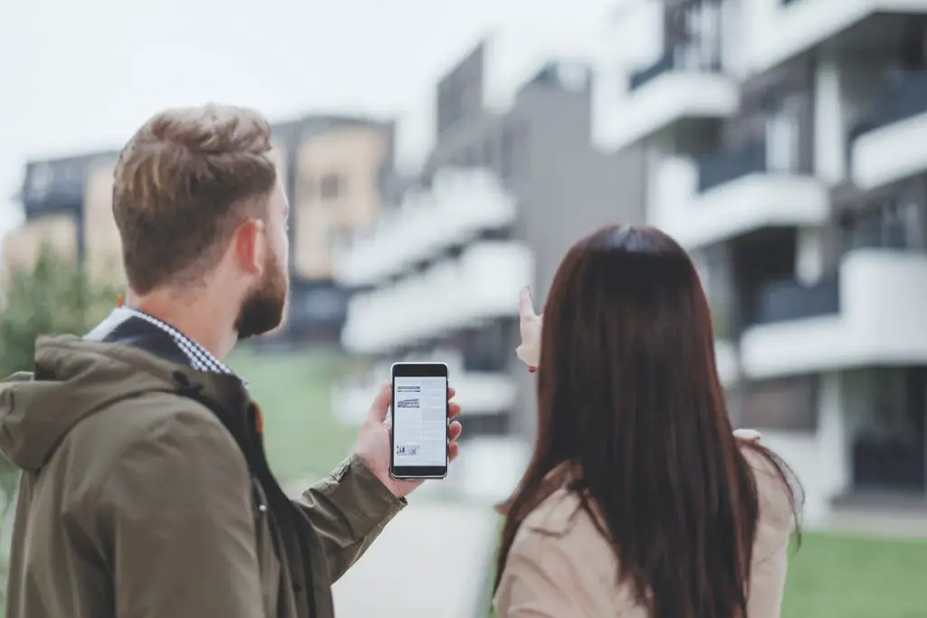 man-and-woman-looking-at-apartment-complex-while-using-online-listing-displayed-on-smartphone