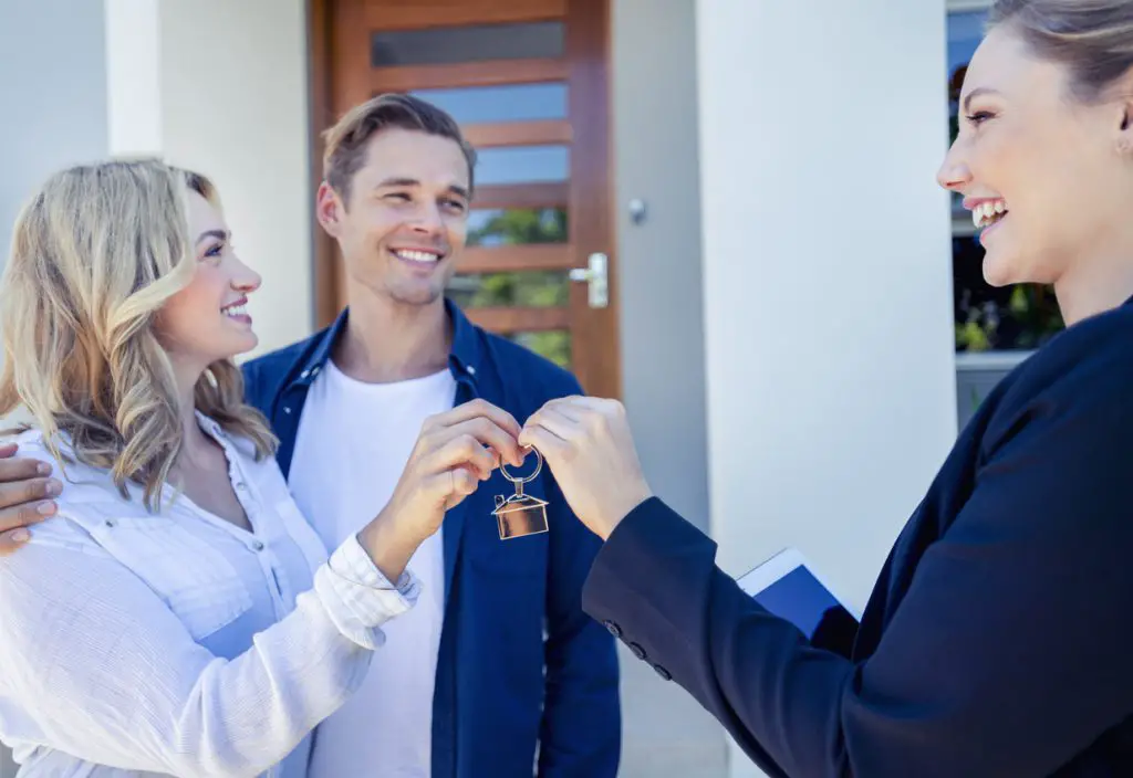happy-couple-receiving-keys-to-new-apartment-from-smiling-landlord