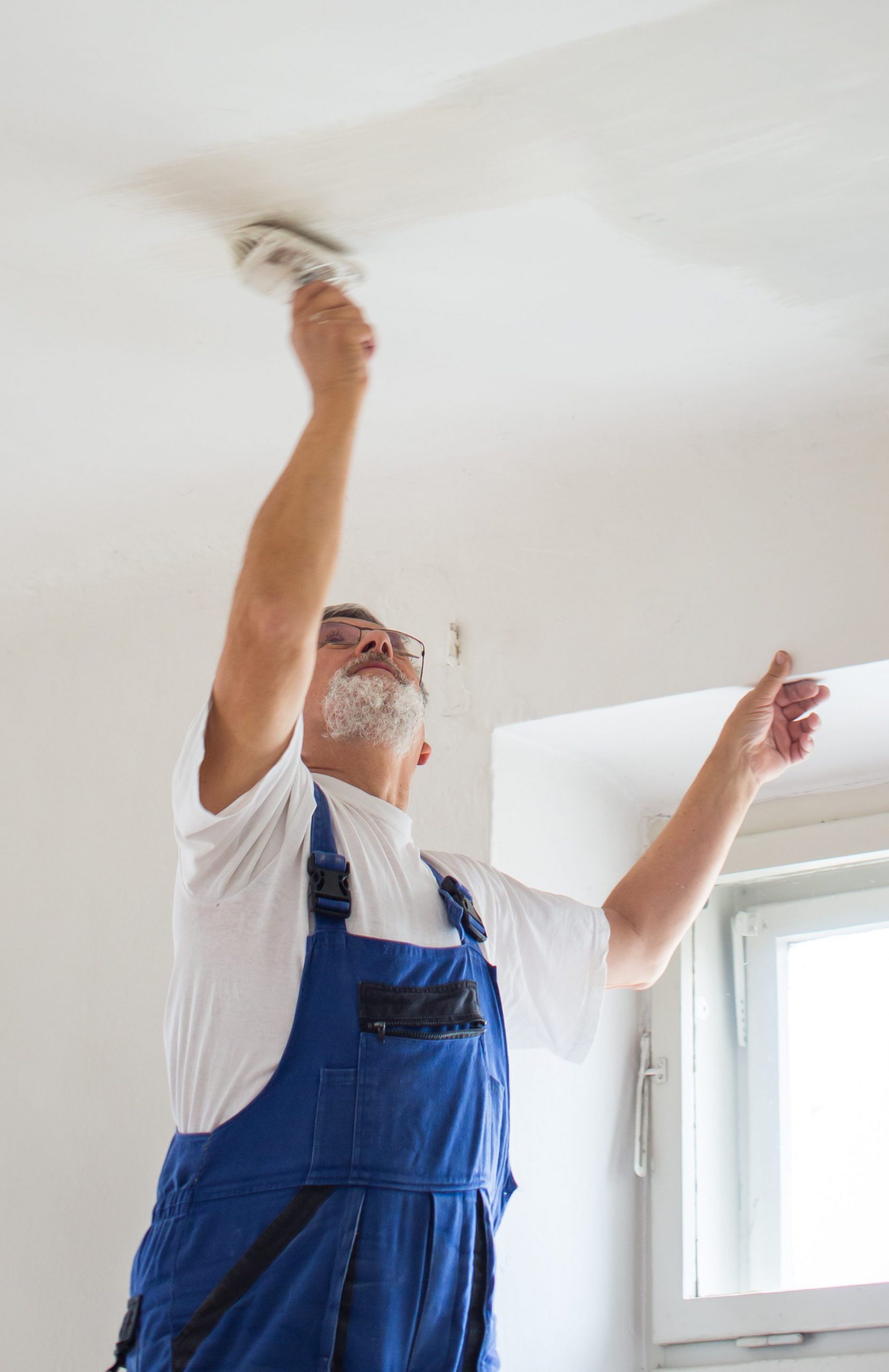 Senior man paintinga room of rental appartment with a paint bucket, wall painting concept - short time rental property maintenance